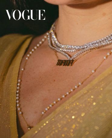 Close-up of layered necklaces with a 'MAMA' pendant on a glittery gold dress.
