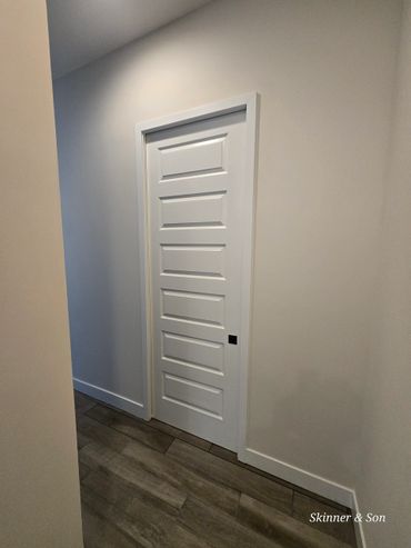 A modern white paneled door in a minimalist hallway with wood flooring.