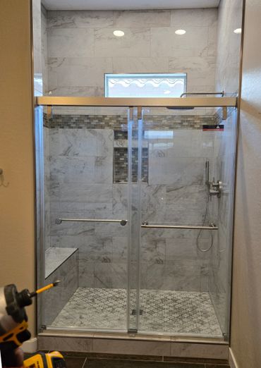 Modern tiled shower with glass doors and built-in bench.