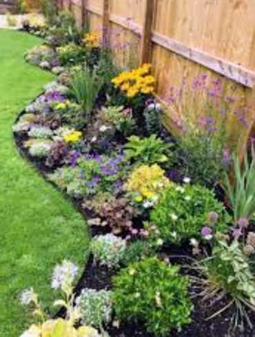 Colorful flower bed along a wooden fence in a garden.