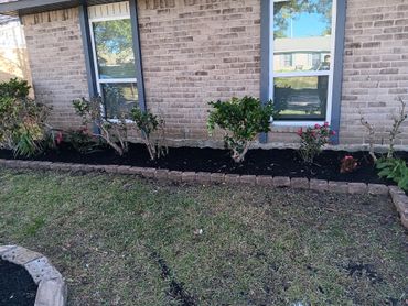 A neat garden bed with shrubs and flowers along a brick house.