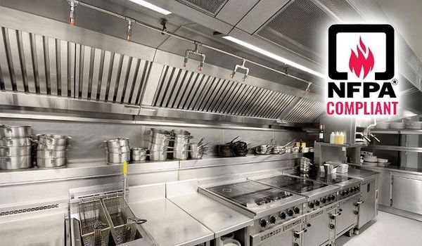 A commercial kitchen with stainless steel appliances and NFPA compliance sign.