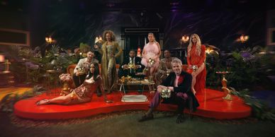 Group of seven people posing on a stylish stage with plants and warm lighting.