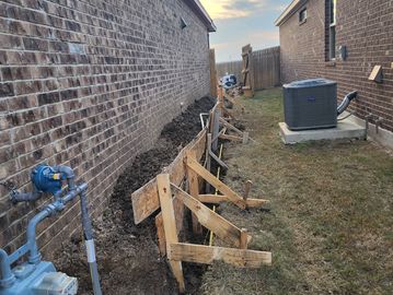 Wooden forms set up along a trench between two houses for concrete pouring.