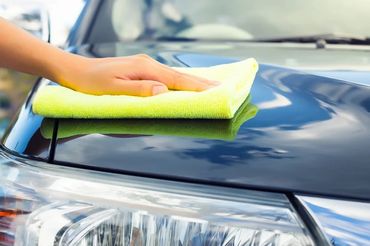 Hand cleaning a shiny black car hood with a yellow cloth.