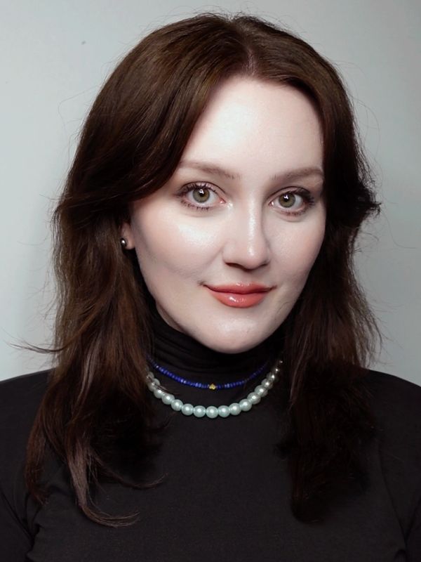 Portrait of a woman with brown hair and pearl necklace against a plain background.