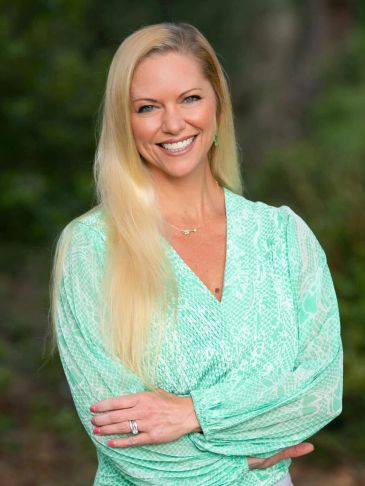 Smiling woman in a mint green blouse outdoors with crossed arms.