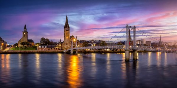 Aerial view of the River Ness with a footbridge crossing, and a historic church in the background.