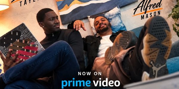 Two men relax on a couch, one reading and the other reclining.