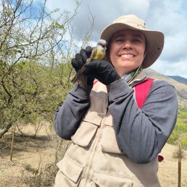 Persona sonriente sostiene un pájaro pequeño al aire libre.