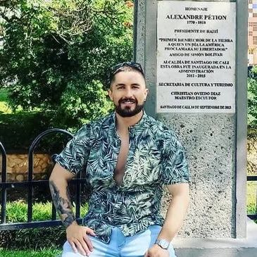 Hombre posa frente a un monumento con placa conmemorativa.