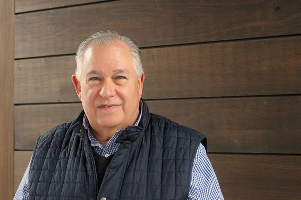 Smiling older man in a quilted vest against a wooden wall.