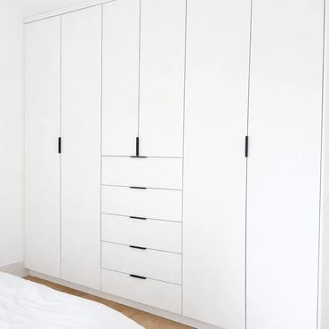 Modern white wardrobe with drawers and black handles.
