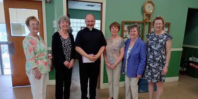 Eine Gruppe von sechs Personen, darunter ein Priester, in einem Raum.