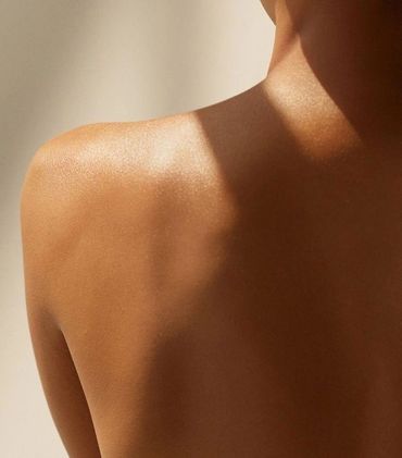 Close-up of a smooth, sunlit human shoulder and upper back.