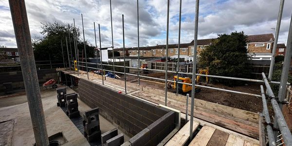 Construction site with brick walls and scaffolding under a cloudy sky.