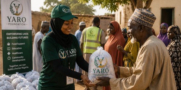 A woman from YARO Foundation hands a food package to an elderly man in a community setting.