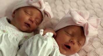 Two newborn babies wearing matching hats with bows, sleeping peacefully.