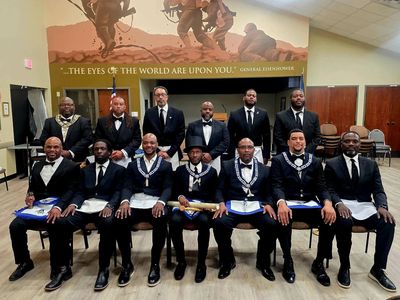 A group of men in formal attire posing indoors with a mural behind them.