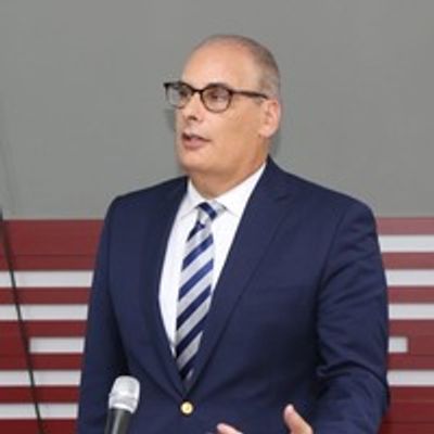 Man in suit speaking, standing behind a microphone.