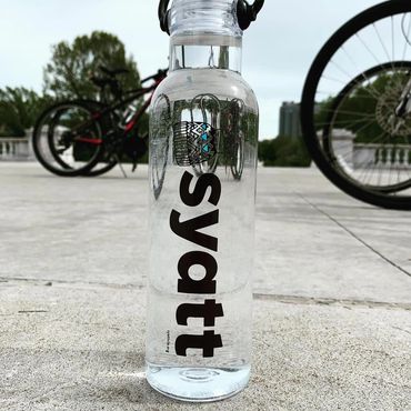 A custom water bottle labeled Syatt on the ground near bicycles.