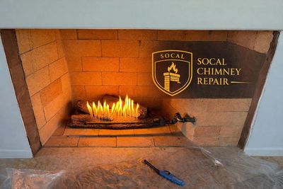 Lit indoor gas fireplace with SoCal Chimney Repair logo on brick wall.