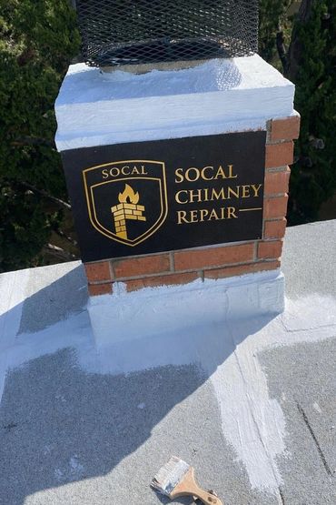 A repaired chimney with a SoCal Chimney Repair sign and a brush on the roof.