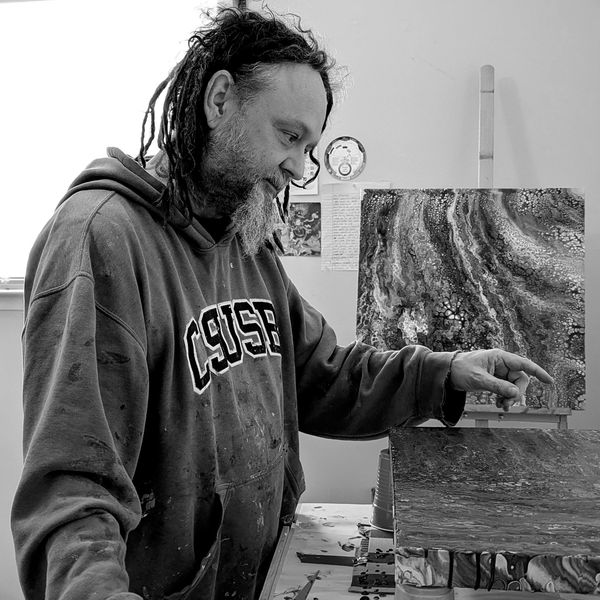 Artist in a CSUSB hoodie working on a fluid painting in a studio.
