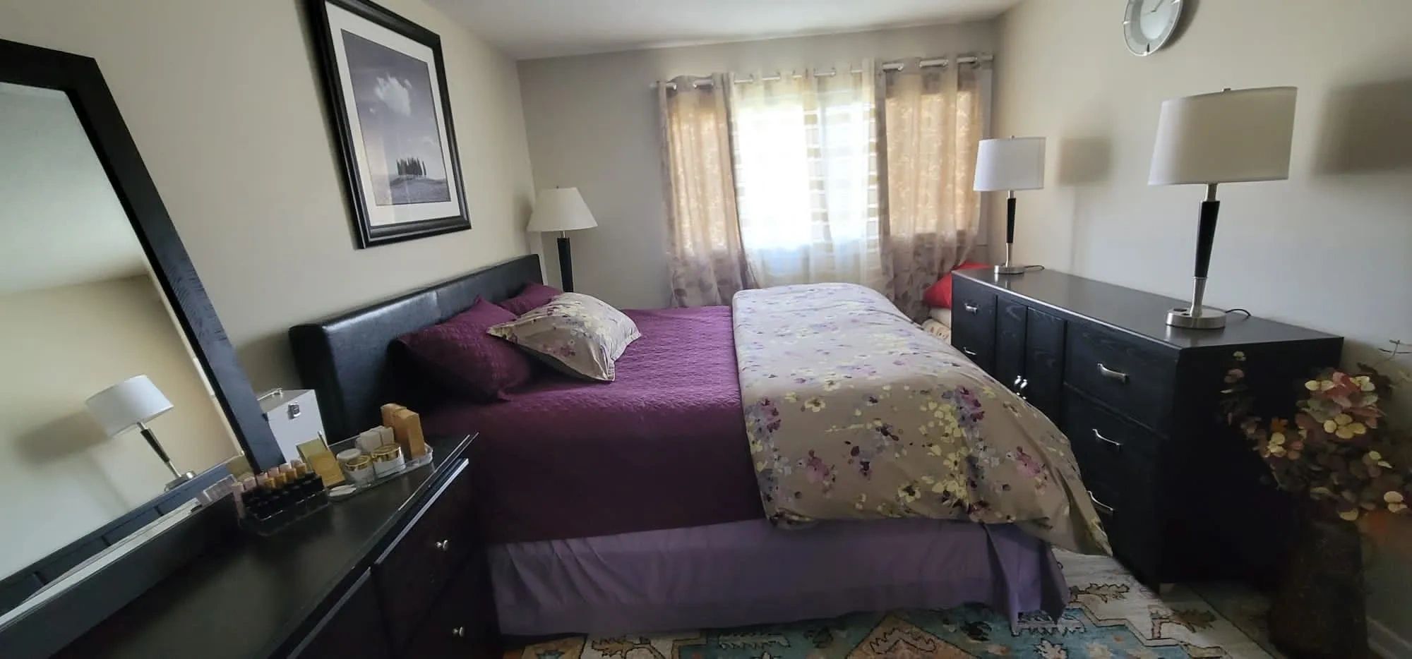 Bedroom : 2 dressers, king size bed purple linen, large mirror, 3 lamps, picture above the bed.