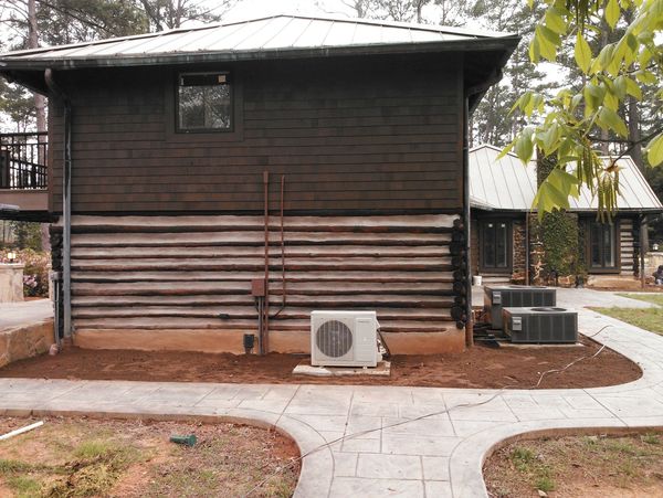 Side view of a log cabin-style house with new landscaping, air conditioning units, and a stone