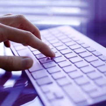 An image of a hand typing on a modern keyboard on a glass table