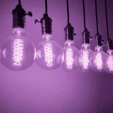 A photo of six retro lightbulbs in a row, each lit with a purple glow