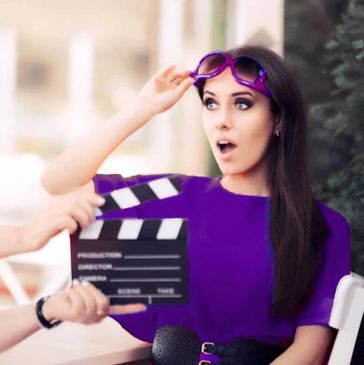An image of an actor with long dark hair, the clapper in the forefront as they film a scene