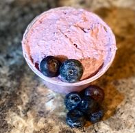 Blueberry flavored whipped cream with fresh blueberries in a plastic cup sitting on a printed table.