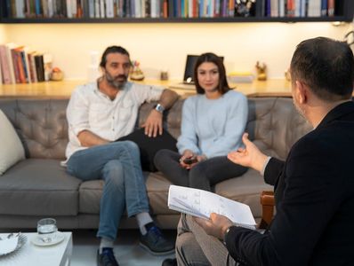 A counselor is seen giving guidance to a couple sitting on a couch during a therapy session. 