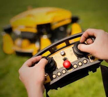 Hands controlling a yellow lawn mower with a remote.