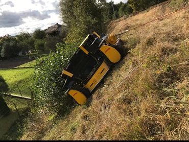 A yellow Spider remote-controlled mower working on a steep grassy slope.