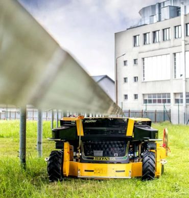 A yellow robotic lawn mower cutting grass near a metal fence.