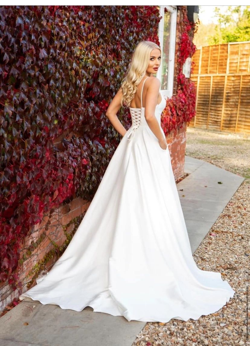 bride in a full skirt bridal gown in mercado satin with pockets, lacced up back fitted plunged neck