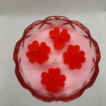Pink candle with red heart-shaped decorations in a red glass holder.