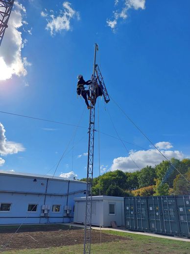 A worker climbs a tall metal tower under a clear blue sky.