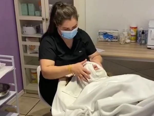 A skincare professional applying a facial treatment to a client wrapped in a white towel.