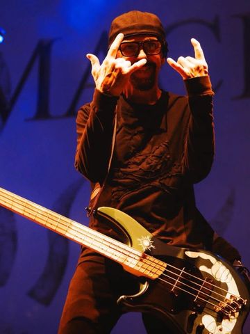 Musician on stage making rock hand signs with electric bass guitar.