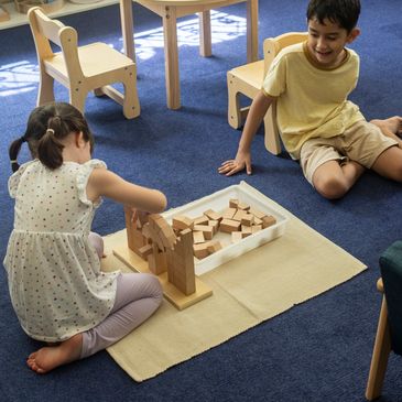 Two kids playing with wooden blocks on a mat.