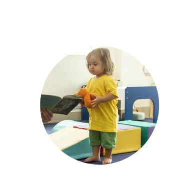 Child in yellow reading with toy.