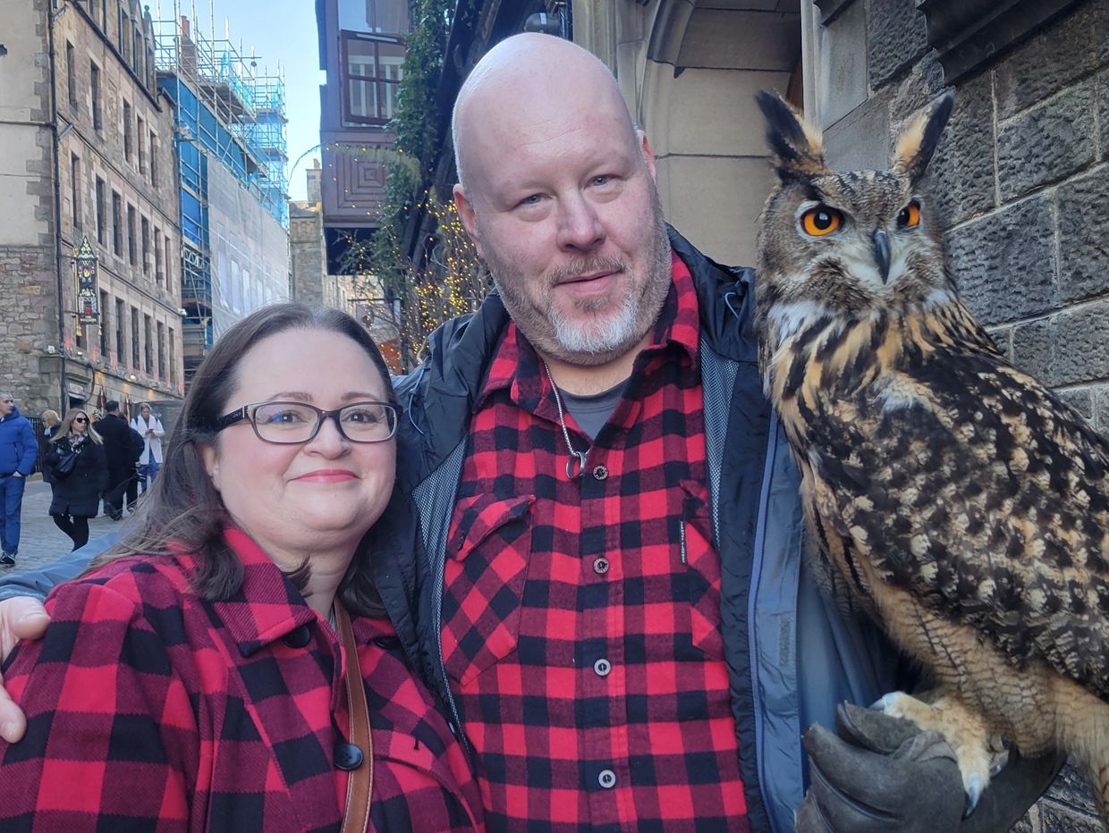 Couple dressed in matching red plaid with an owl on a glove in an urban setting.