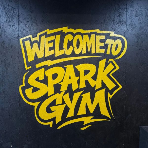 Bright yellow graffiti saying 'Welcome to Spark Gym' on a black wall.