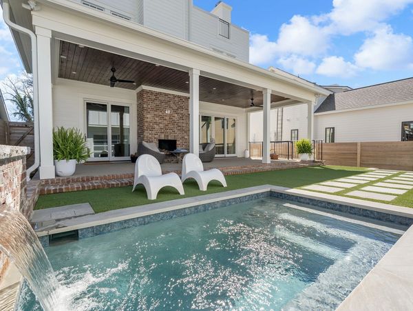 Modern backyard with a pool, waterfall, and white lounge chairs on artificial turf.