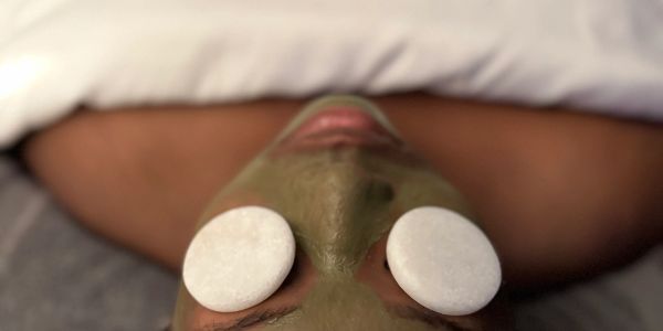 Person lying down with a green facial mask and white cucumber slices on eyes.