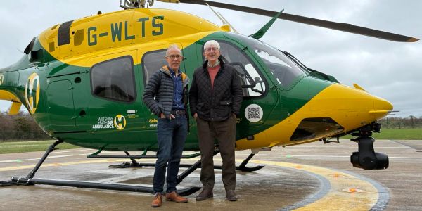 Two men posing in front of a green and yellow helicopter.
